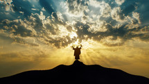 Silhouette of Jesus praying on a hill with mystic clouds behind Him.

