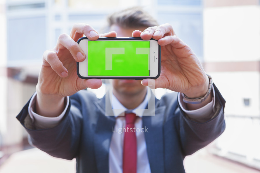 Businessman holding a smartphone to the camera with a green screen- for editorial use only 