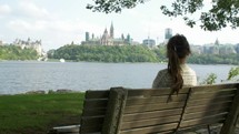 woman sits on bench looking towards parliament of Canada