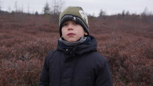 Young boy outdoors on nature walk in late autumn takes deep breath 
