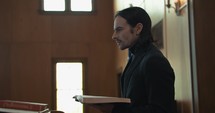 Young pastor in church with bible preaching, teaching sermon to congregation in Sunday morning worship service.