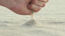 A boy's hand is dropping a pile of sand from the beach