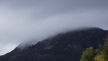 Time-lapse movement of fast clouds across a misty alpine mountain peak. Zoom in