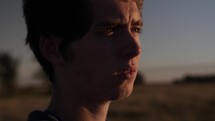Young man, standing in a field alone and watching the sunset or sunrise in cinematic slow motion.