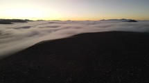Aerial shot drone flies toward fog covered valley just before sunrise
