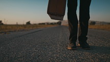 man walking alone on a road carrying a suitcase 