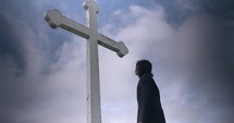 Young man in black suit looking at cross praying in worship in cinematic slow motion.