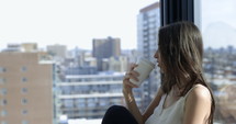 Woman sipping tea as she looks off into city skyline