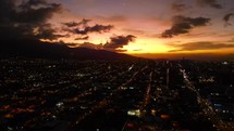 Aerial shot drone flies backwards away from sunset over city