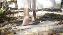 The feet of Jesus Christ or spiritual, angelic figure in white, tattered robe walking in dramatic, cinematic slow motion.
