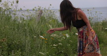 Young woman smelling flowers in meadow by the ocean - side profile 
