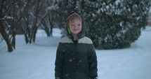 Happy, young boy smiling in cinematic slow motion snow. Young kid playing in snowfall on Christmas morning.