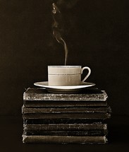 cup of steaming coffee on a stack of old books