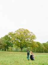 Couple walking through a field with trees.