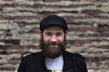 Smiling bearded man standing in front of a brick wall.