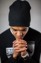 a man in a beanie with head bowed in prayer 