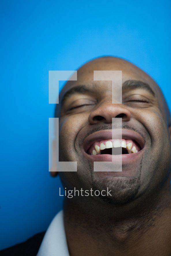 A man with his head thrown back and laughing against a blue background.