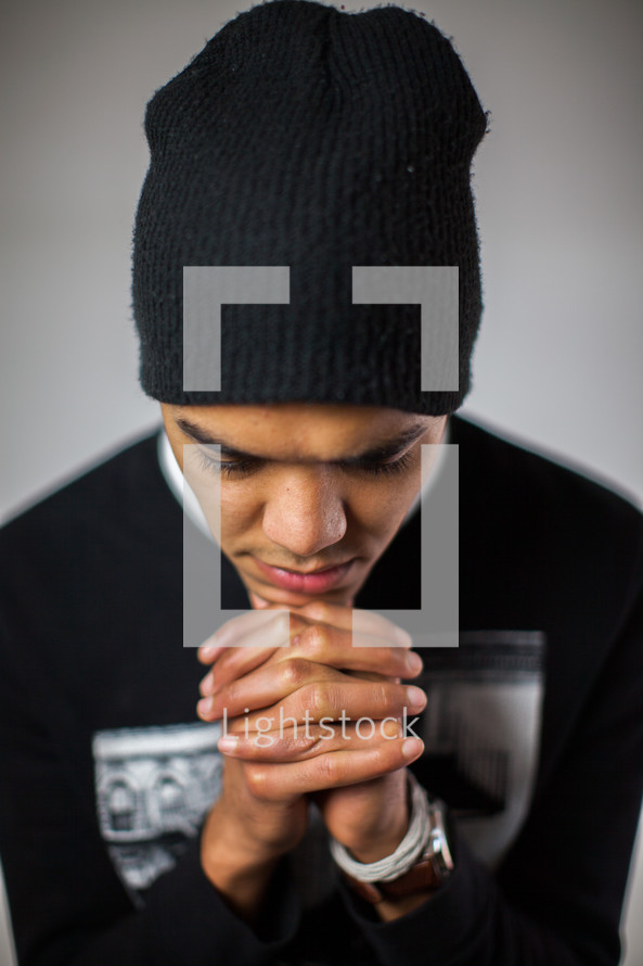 a man in a beanie with head bowed in prayer 
