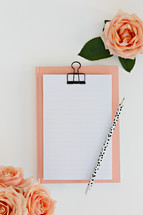 clipboard, pencil, peach roses, and blank paper 