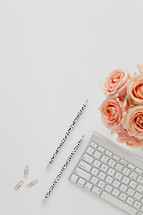 paperclips, computer keyboard, pencils, and peach roses on a desk 