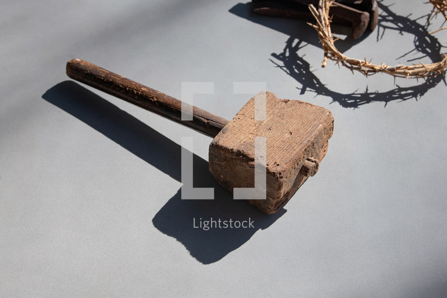 Wooden Mallet, Crown of Thorns and Three Nails with shadows on a grey background