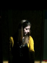 a teen girl looking down standing in darkness