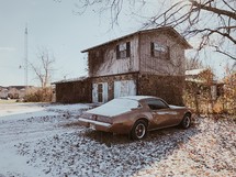a car parked in a driveway beside a house with a dusting of snow 