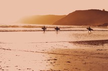 surfers walking on a beach at sunrise 