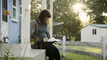 a woman sitting on reading a Bible on a porch 