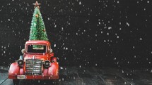 red truck with Christmas tree and falling snow 