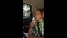 Vertical video - A 12-year-old boy in a striped tank top sits in the back passenger seat of a car, enjoying an ice cream