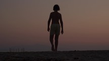 Teenage boy, seen from behind, walks away on a beach at sunset in the evening