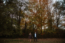 couple holding hands standing in front of a fall forest 