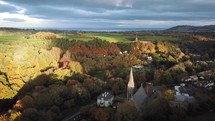 Aerial Pan Over Light on Autumn Trees from Knocksink Wood to Enniskerry Village, County Wicklow, Ireland