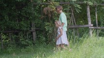 Brother and sister holding hands walking along a wooden fence in a garden setting