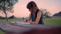 Woman Reading Bible and Journaling Outside at Sunset