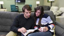 a couple reading a Bible on a couch 
