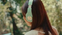 Woman listening to music alone in the park wearing modern headphone, camera approaching from back 