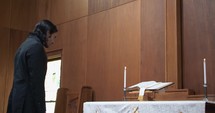 Young Christian man in black suit praying in church, confessing sin and repenting near wooden cross.