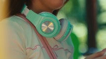 close up of green headphone on the neck of a female woman while standing outdoor waiting for a date , blurred bokeh background 