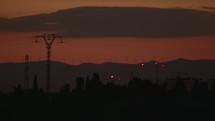 Power lines at sunset. Electric poles and high voltage lines against the background of trees and wind turbines standing on a hill in the distance