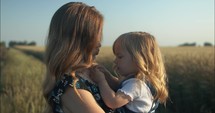 Mother kissing her young daughter in summer sunset.