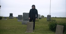 Young, sad man in black suit kneeling in cemetery at graveyard tombstone grieving in cinematic slow motion.