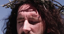 A crown of thorns placed on Jesus' head, blood flows down.