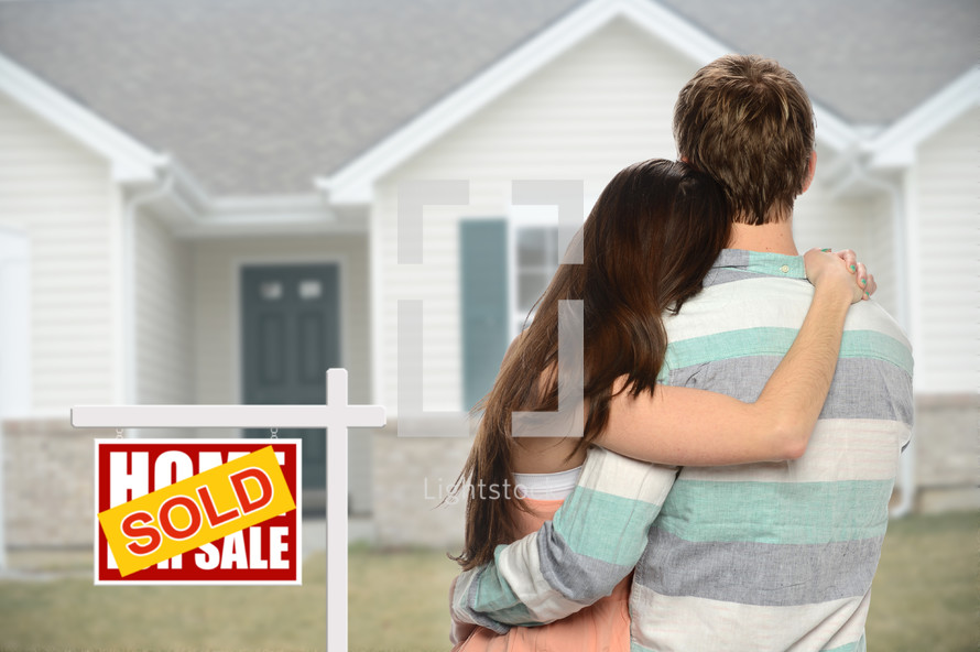 couple standing next to a sold sign in front of their new home