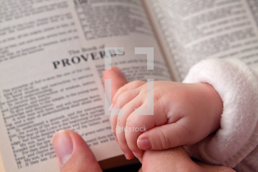 infants hand over mother's fingers and an open Bible