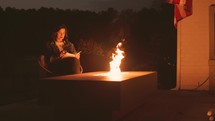 Woman Reading Bible by a Fire at Night