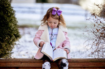 girl in a pink coat reading a Bible outdoors 
