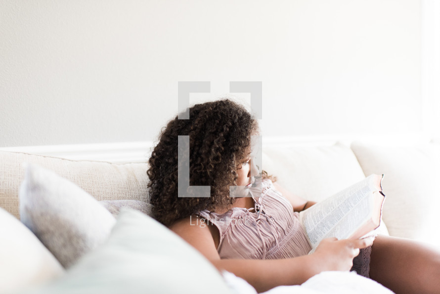 teen girl reading a Bible on a couch 