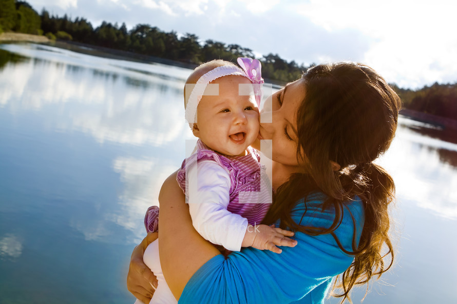mother kissing her baby by a lake